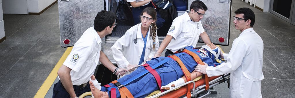 Foto estudiantes realizando proceso de atención prehopitalaria con simulador de ambulancia y paciente.